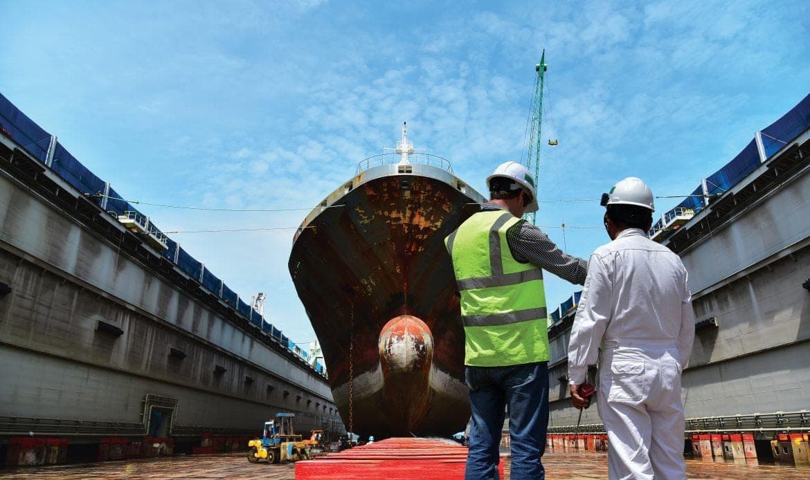 Two surveyors walking towards a vessel raised in a floating dry dock