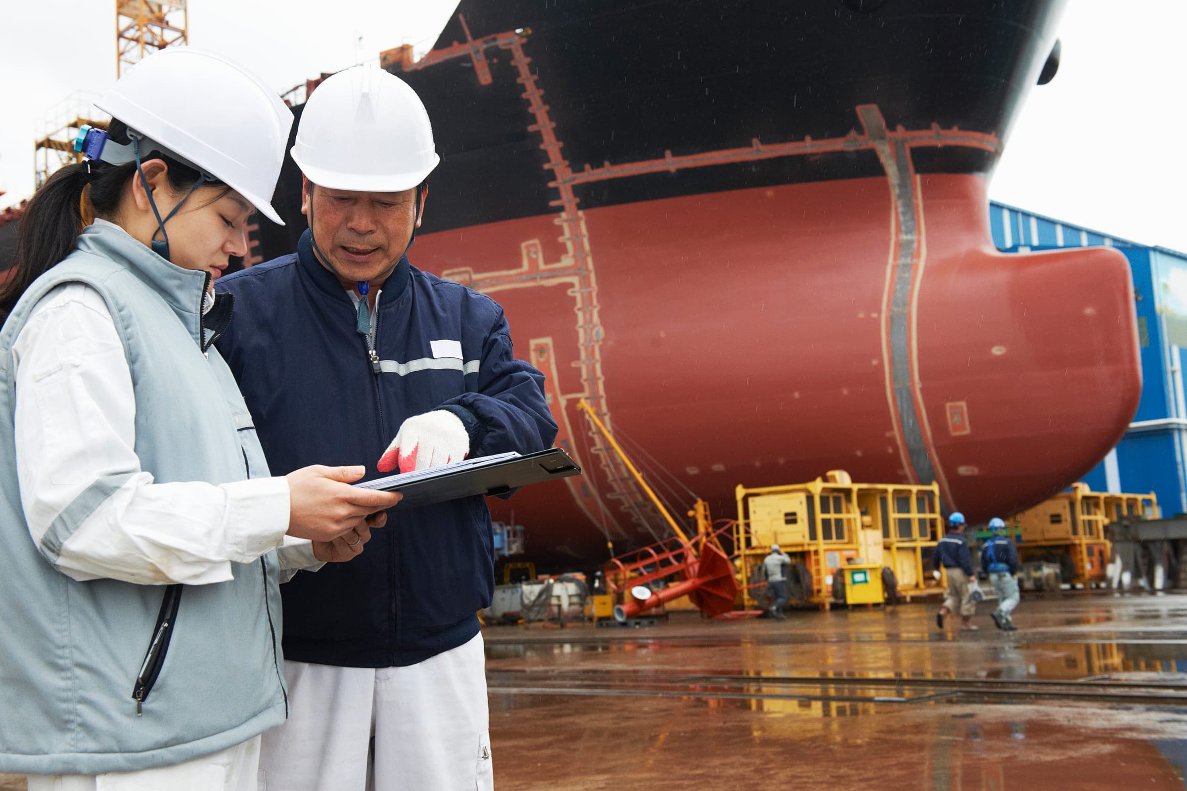 Two surveyors reviewing findings in front of a vessel hull